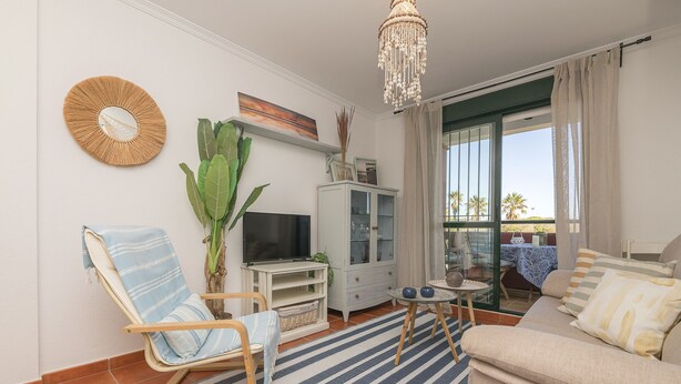 A living room with a sofa, a TV, a chandelier, and a view of the outdoors. - Marina Place in Chiclana de la Frontera (Chiclana de la Frontera)