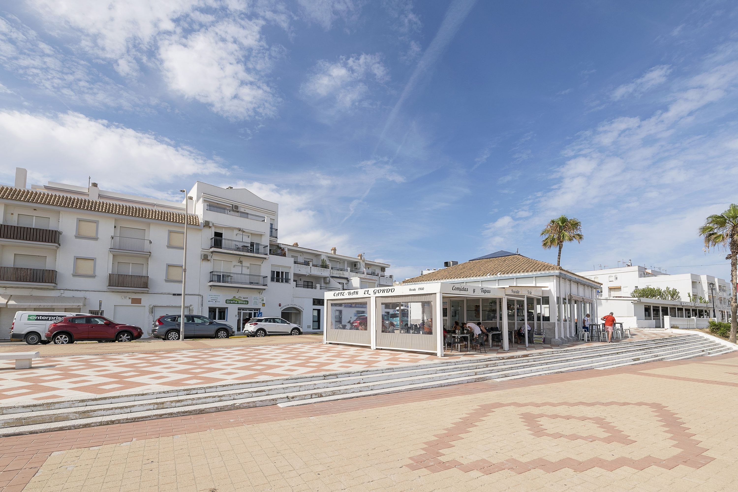 A cafe with outdoor seating, a checkered pavement, and a clear sky.