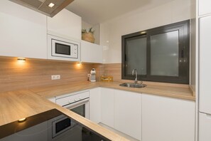 A modern kitchen with white cabinetry, a wooden countertop, a built-in microwave, and a window with frosted glass. - La Yerbabuena in Barbate (Barbate)