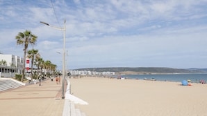 Una playa con un paseo marítimo empedrado, palmeras y sombrillas de playa.