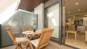 Un comedor con mesa y sillas de madera, un separador de vidrio y vistas hacia una zona de cocina.