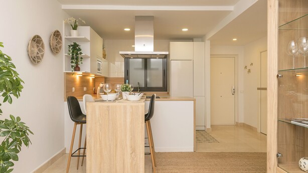 Una cocina moderna con una isla central, armarios blancos y un horno empotrado.