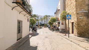 Una calle adoquinada bordeada de edificios, un café con terraza y un cielo azul despejado.