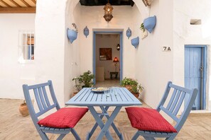 Ένα μπλε τραπέζι με δύο καρέκλες, κόκκινα μαξιλάρια και μια λευκή πόρτα με τον αριθμό 7Α.