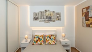 Un dormitorio con una cama, dos mesitas de noche, una obra de arte en la pared y suelo de madera.