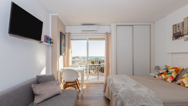 Un dormitorio moderno con sofá, cama, televisor y balcón con vistas a la ciudad.