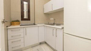 Una piccola cucina moderna con mobili bianchi, un lavello incassato e una finestra sopra il piano di lavoro.