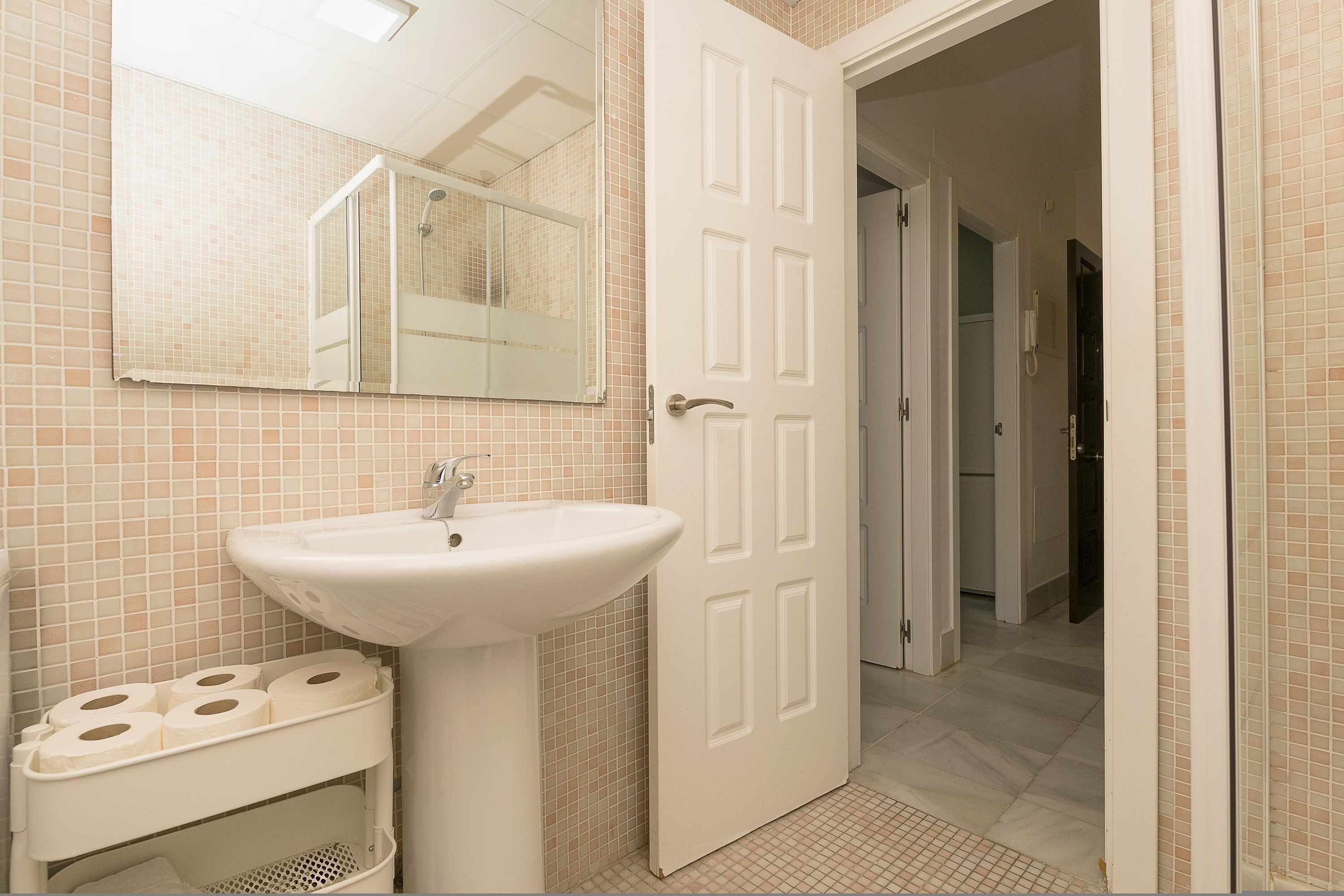 A bathroom with a sink, toilet paper holder, and a door leading to another room.