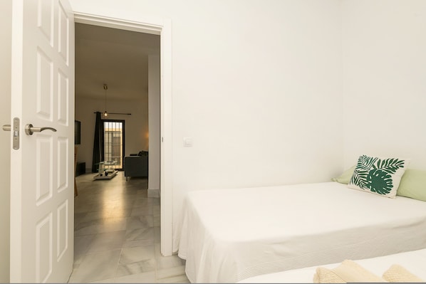 A bedroom with a bed, a door, and a hallway leading to another room.