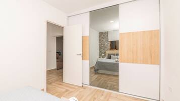 Un dormitorio con puerta corredera para el armario, una cama con colcha gris y suelo de madera.