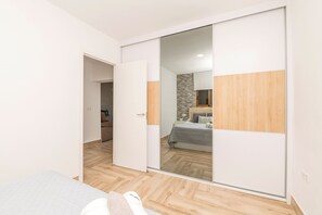 A bedroom with a sliding closet door, a bed with a grey quilt, and a wooden floor. - Casa Roja in La Ribera de la Oliva (Vejer de la Frontera)