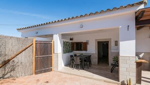 Un edificio blanco con tejado de tejas, cerca de madera y un patio con mesa y sillas.