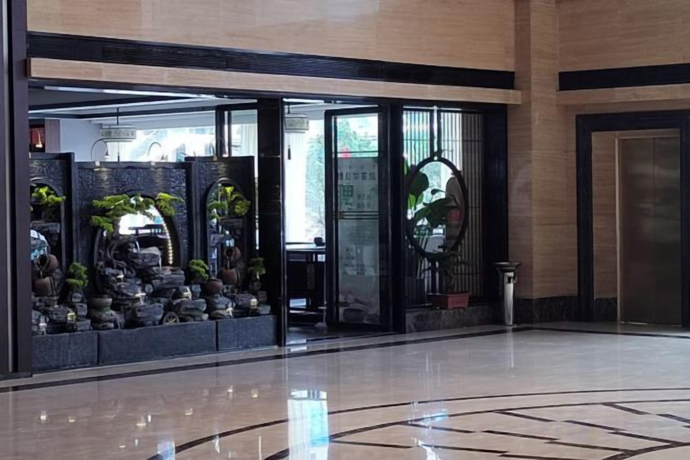 A lobby with a glass entrance, a reception desk, and a decorative plant arrangement.