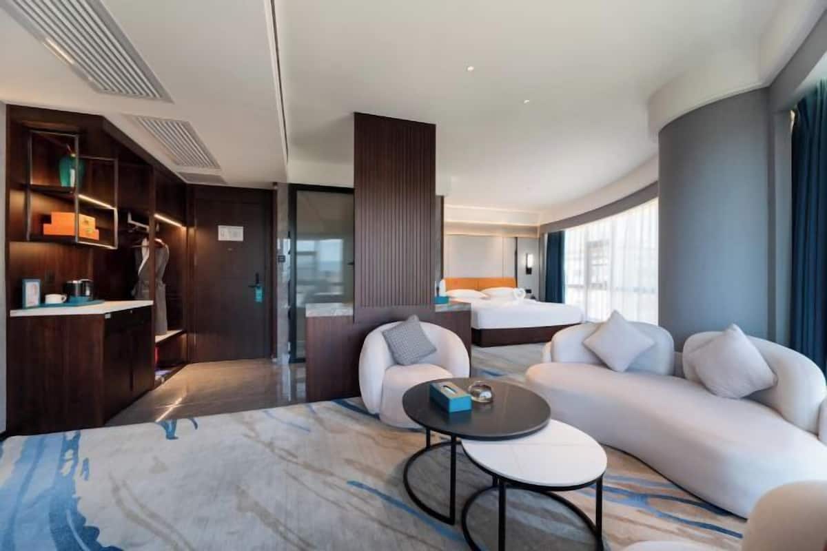 Quarto de hotel moderno com cama grande, sofá, mesa de centro e armário embutido.