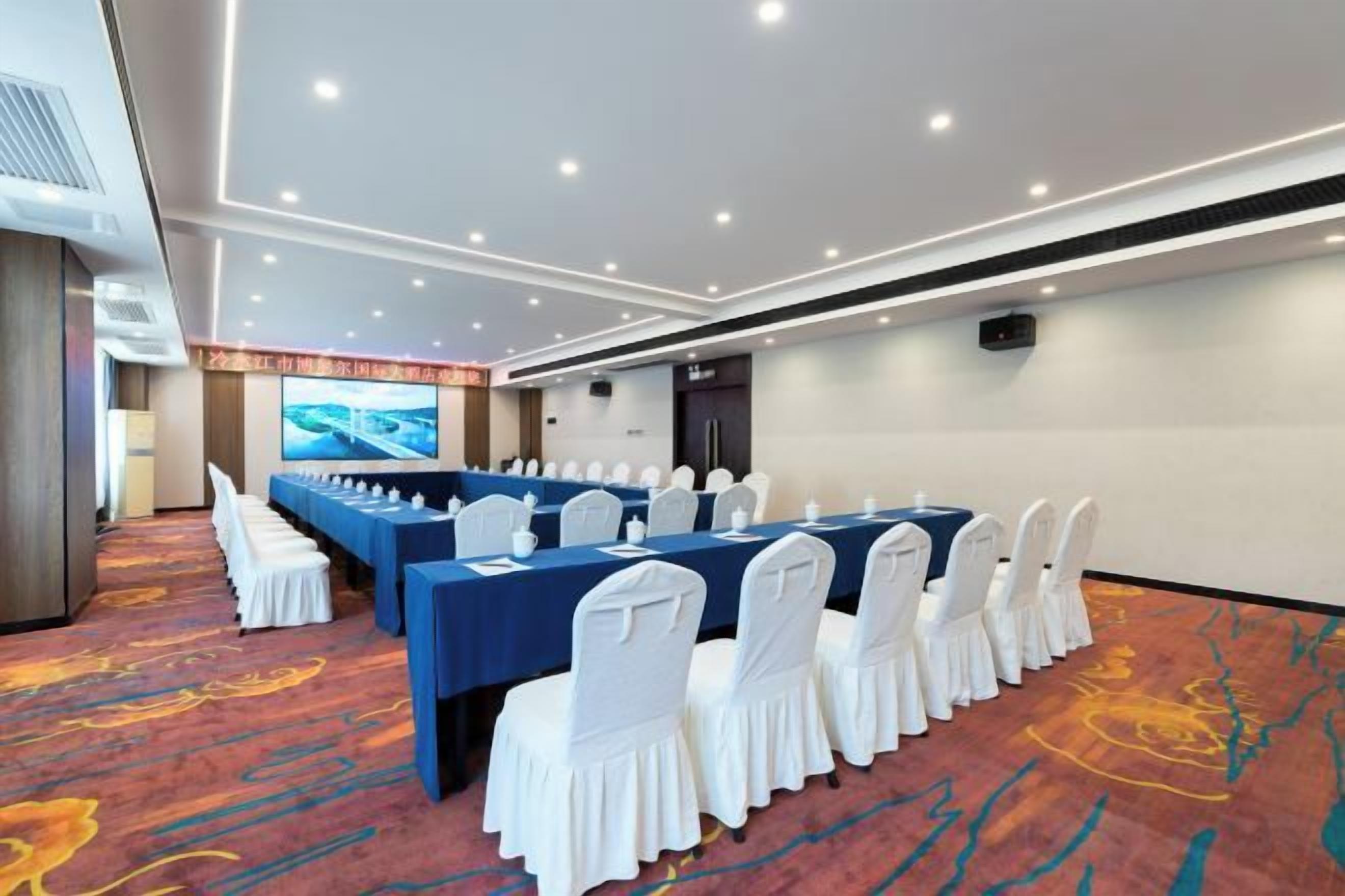 A conference room with a long table, white chairs, and a carpeted floor.