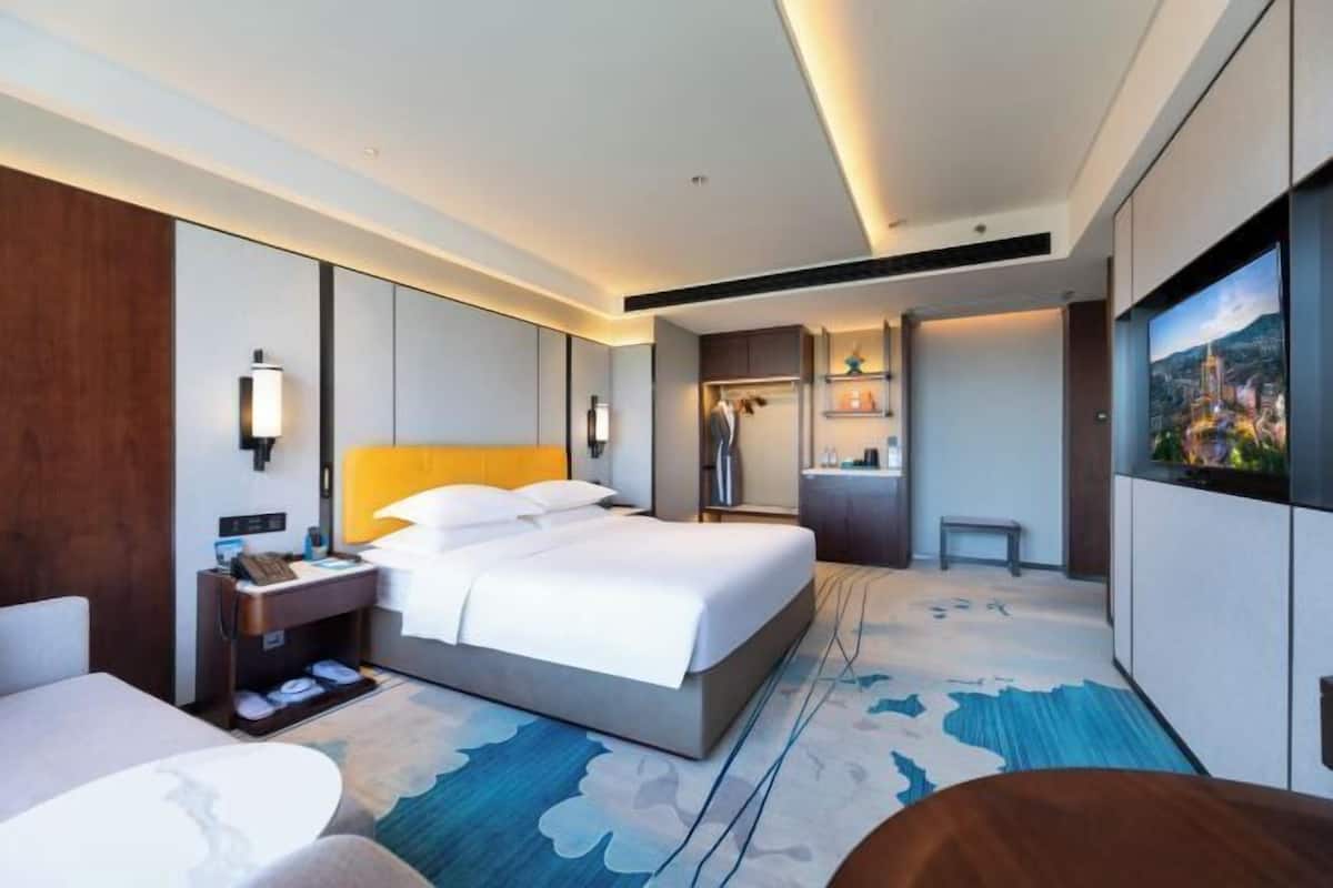 Quarto de hotel com cama, mesa de cabeceira, luminária e vista para a cidade.