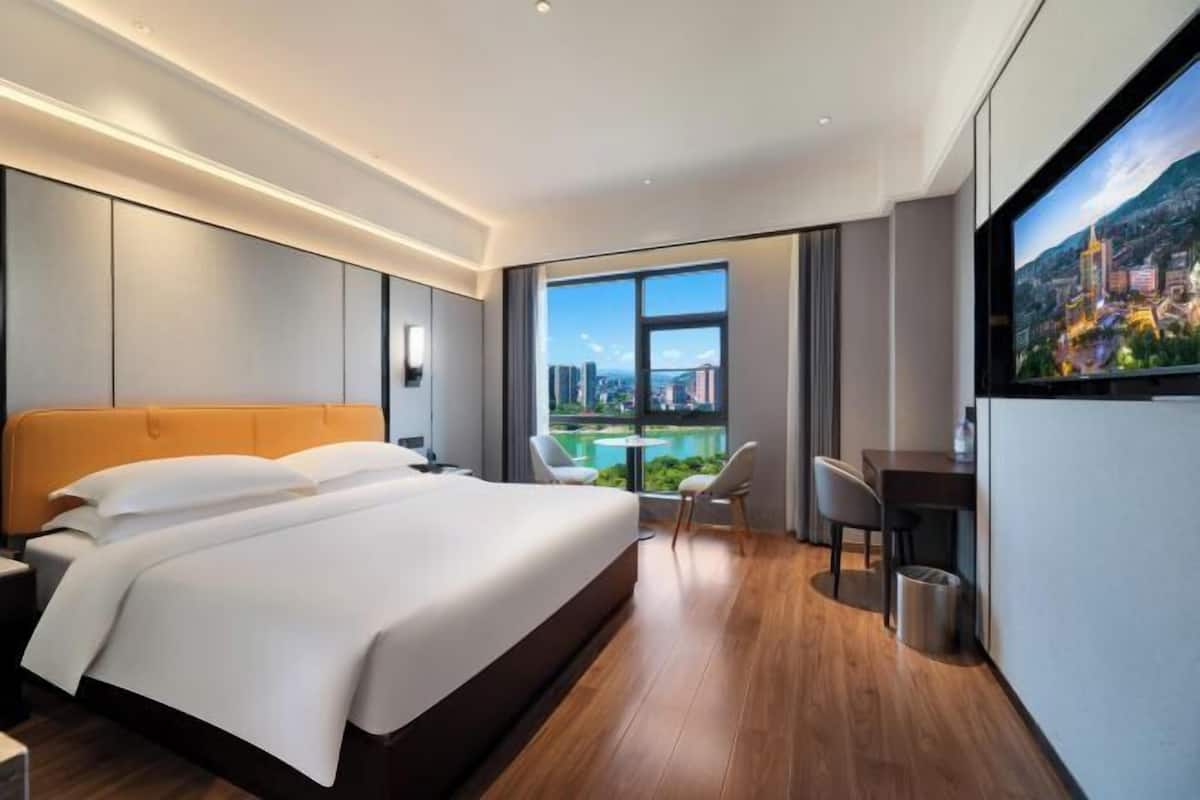 Quarto de hotel moderno com uma cama grande, uma escrivaninha e vista para a paisagem urbana.