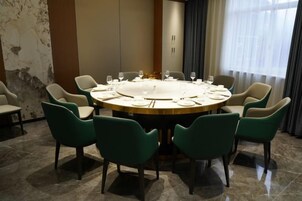 A round table with chairs, a chandelier, and a window with curtains.