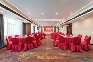 Un salón de conferencias con mesas redondas y sillas, piso alfombrado y un ventanal grande en un lateral.