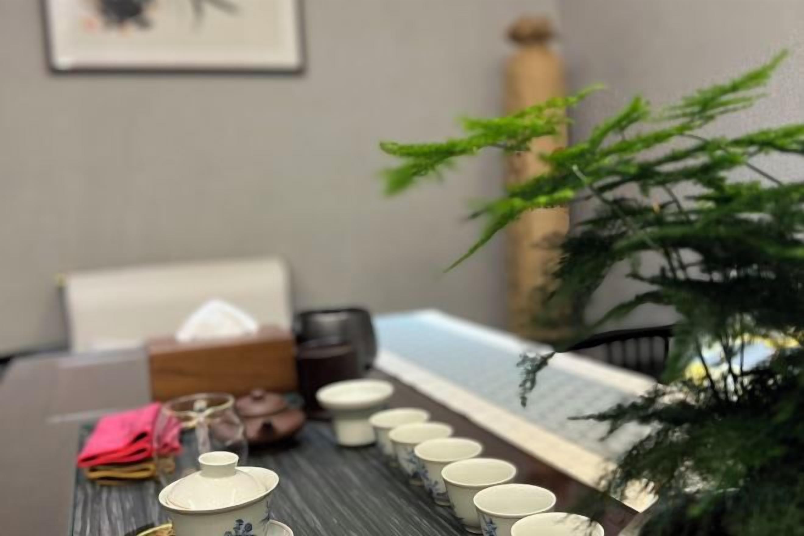 A dining table with a set of teapots and cups, a plant, and a chair.