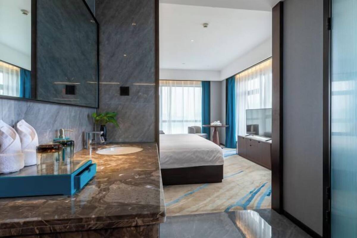 Quarto de hotel moderno com casa de banho em mármore, uma cama grande e vista para a cidade.