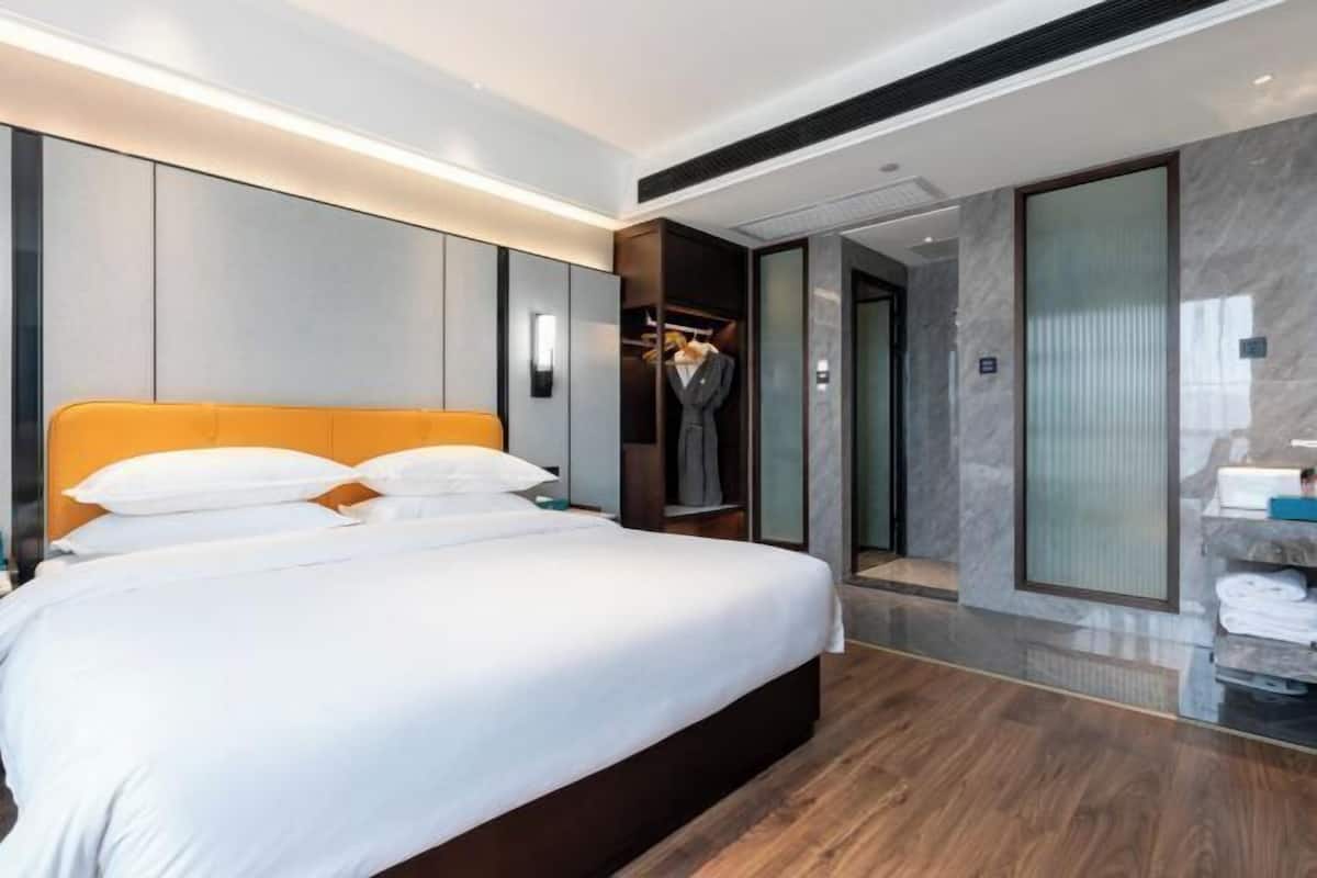 Quarto de hotel moderno com uma cama grande, um guarda-roupa, um espelho e um banheiro visível através de uma porta aberta.