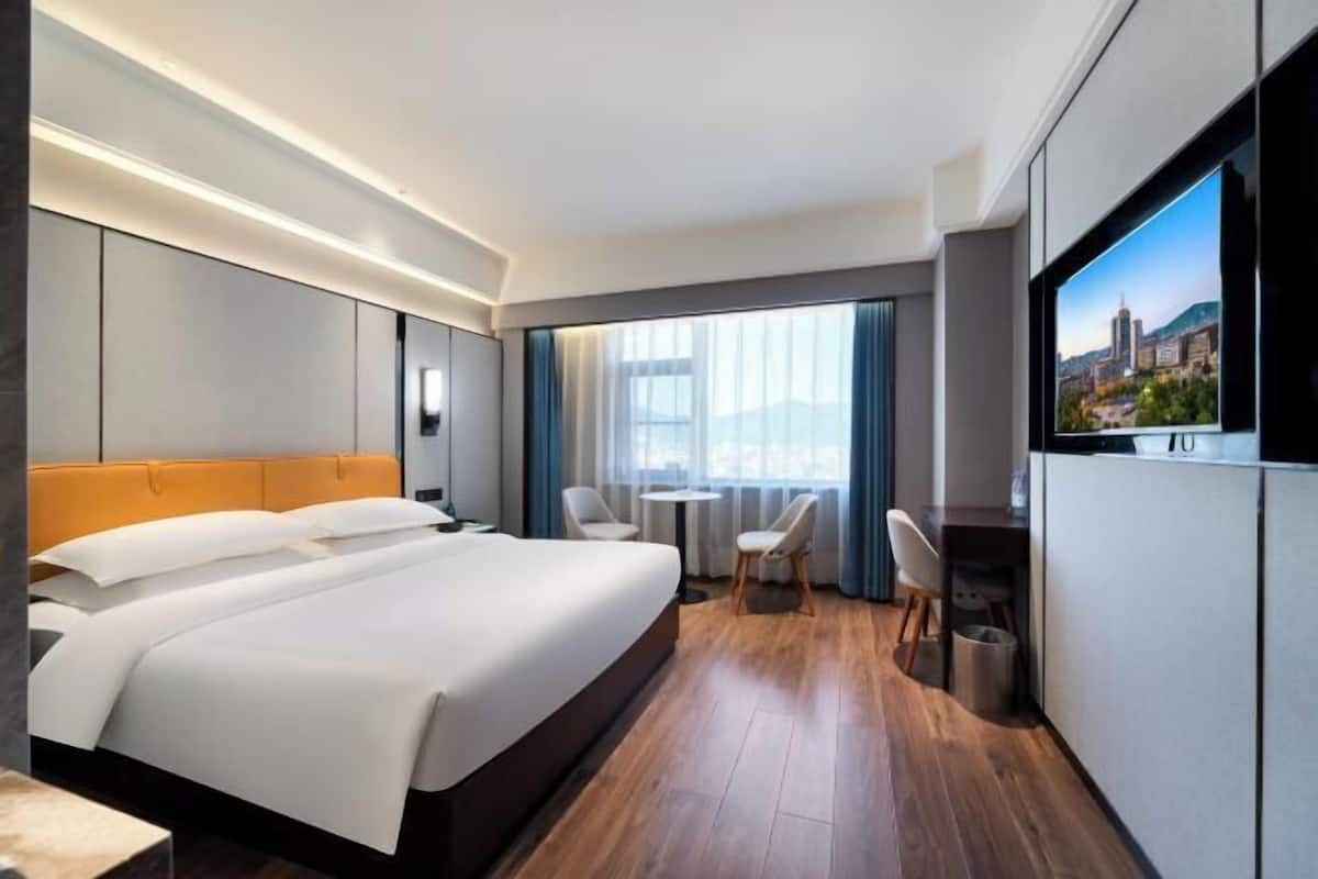 Quarto de hotel moderno com uma cama grande, uma escrivaninha e uma televisão.