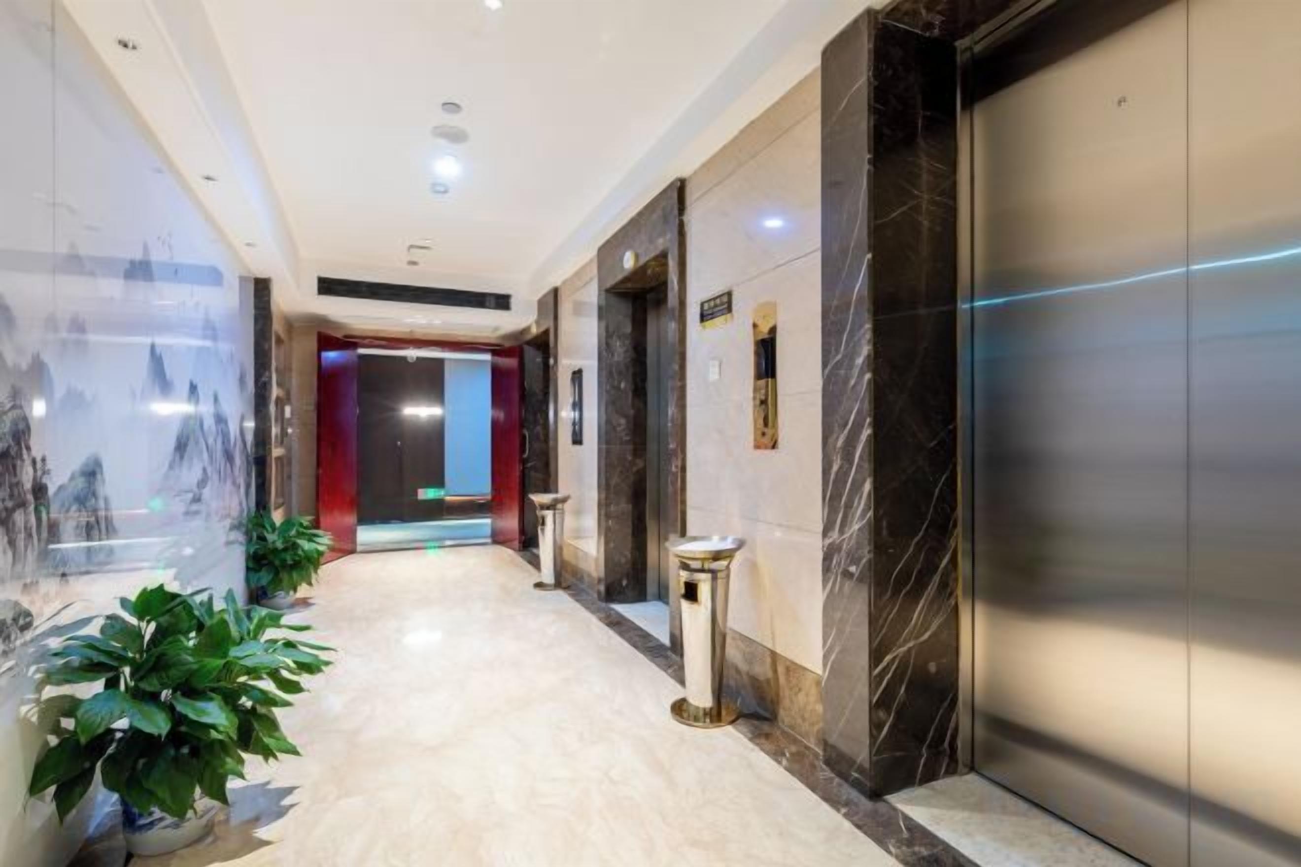 A hotel corridor with a marble floor, a glass wall with artwork, and a red door at the end.