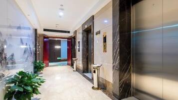 A hotel corridor with a marble floor, a glass wall with artwork, and a red door at the end.
