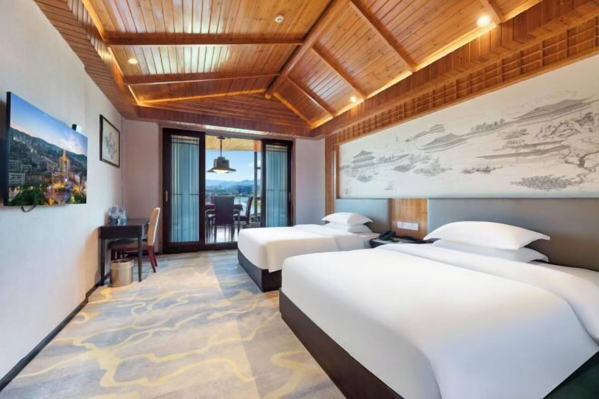 Quarto de hotel com duas camas, um espaço de refeições e uma janela grande com vista.