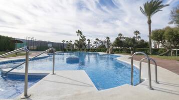Piscina con barandillas metálicas, rodeada de palmeras y un cielo despejado.