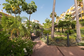 A pathway leading to a building with a gated entrance, surrounded by lush greenery and palm trees. - Calanova in Urbanizaci n Riviera Sol (Mijas)