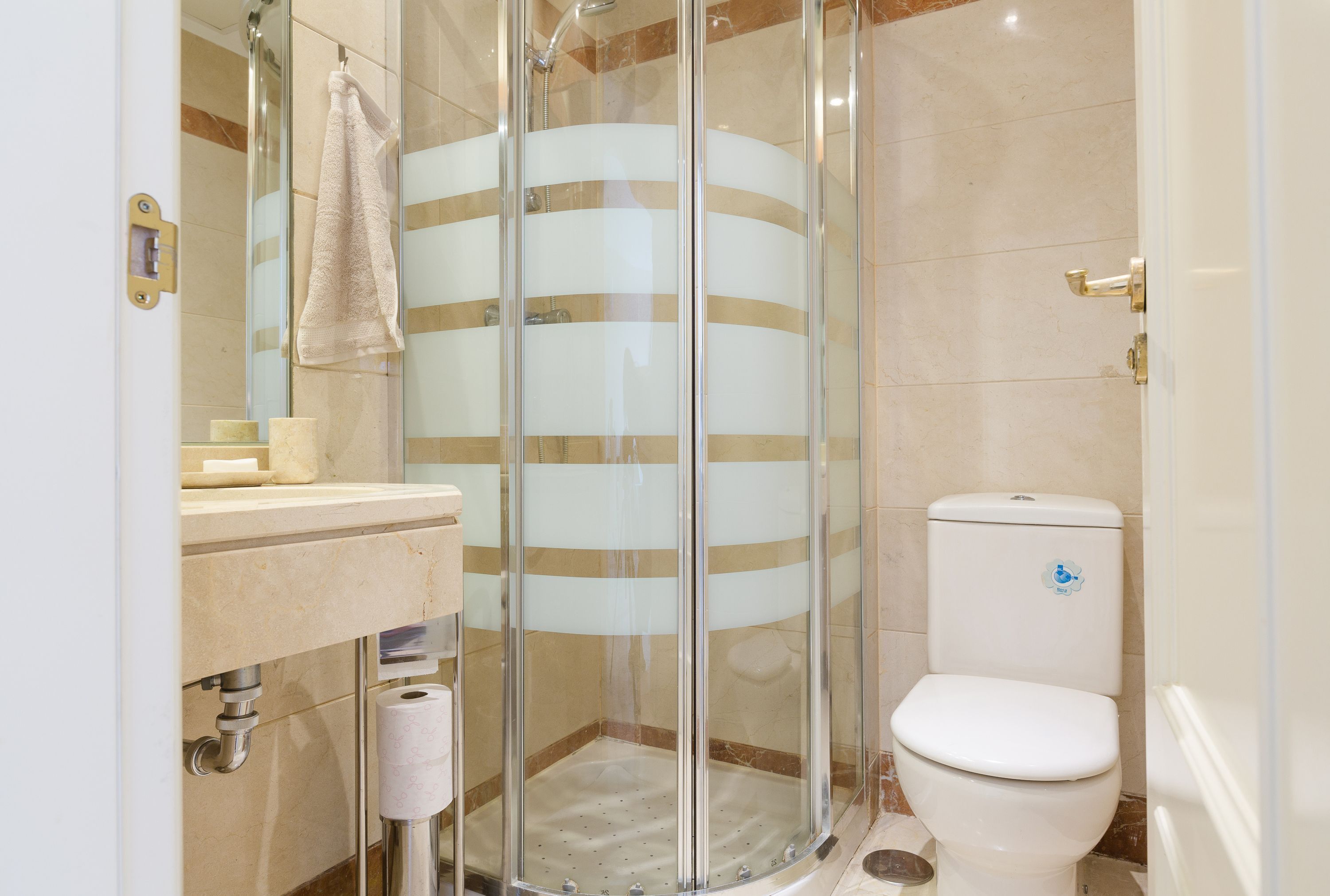 A modern bathroom with a glass-enclosed shower, a toilet, and a sink with a towel hanging on the wall.