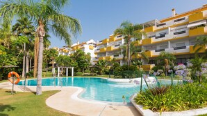 Una piscina circondata da palme e un edificio con balconi gialli e bianchi.
