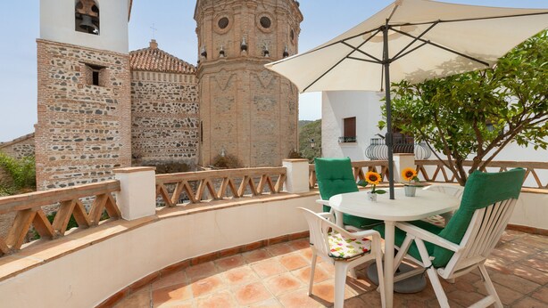 Una terrassa amb taula i cadires blanques, un gran para-sol i vista d'un edifici històric amb una torre del campanar.