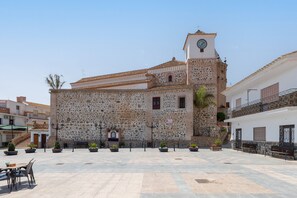 Un patio con edificios de piedra, una torre de reloj y mobiliario exterior.
