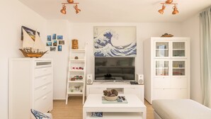 Un soggiorno moderno con un grande televisore, mobili bianchi e un dipinto raffigurante un’onda giapponese.