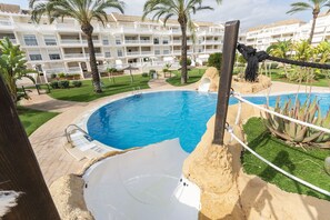 A swimming pool with a rope barrier, palm trees, and a building with balconies in the background. - Aquamarinas in D nia (Denia)