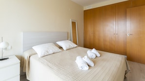 Una cama bien hecha con ropa de cama y almohadas blancas, una mesita de noche con lámpara y un armario de madera.