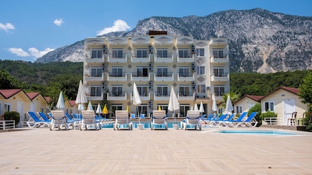 A hotel with multiple balconies, a swimming pool, and a mountainous backdrop.