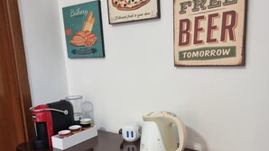 Keittiön työtasolla on kahvinkeitin, vedenkeitin ja keksejä sisältävä rasia. Seinällä on kolme kehystettyä kylttiä: yksi, jossa mainostetaan pizzaa, toinen, jossa mainostetaan leipomotuotteita, ja kolmas, jossa ilmoitetaan, että huomenna on tarjolla ilmaista olutta.