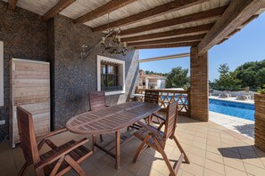 An outdoor patio with a wooden table and chairs, a stone wall, and a view of a swimming pool. - Villa Lina in Estepona (Estepona)