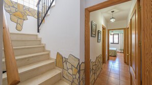 A staircase with stone accents, a wooden handrail, and a view into a room with a bed and a window. - Villa Lina in Estepona (Estepona)