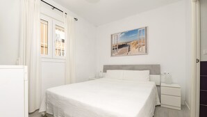 A bedroom with a large bed, a nightstand, a wall-mounted painting, and a window with curtains. - Retiro Al Amanecer in Chiclana de la Frontera (Chiclana de la Frontera)