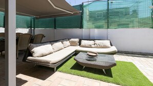 A covered outdoor seating area with a sectional sofa and a round table, surrounded by chairs and a green artificial turf. - Retiro Al Amanecer in Chiclana de la Frontera (Chiclana de la Frontera)