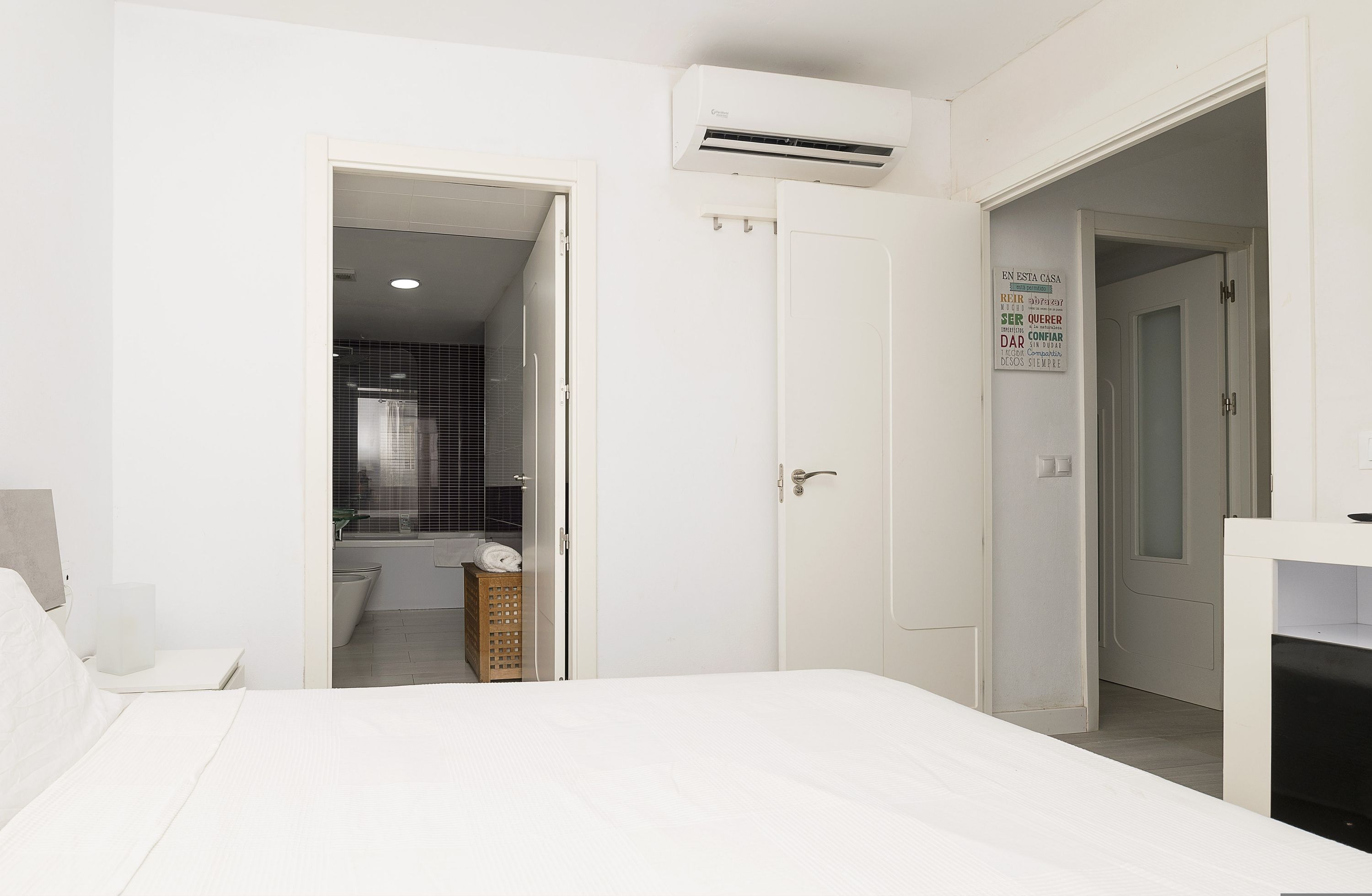 A bedroom with a bed, a white wardrobe, and an air conditioning unit.