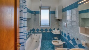 Et badeværelse med badekar, toilet og vask, med blå og hvide fliser samt et vindue.
