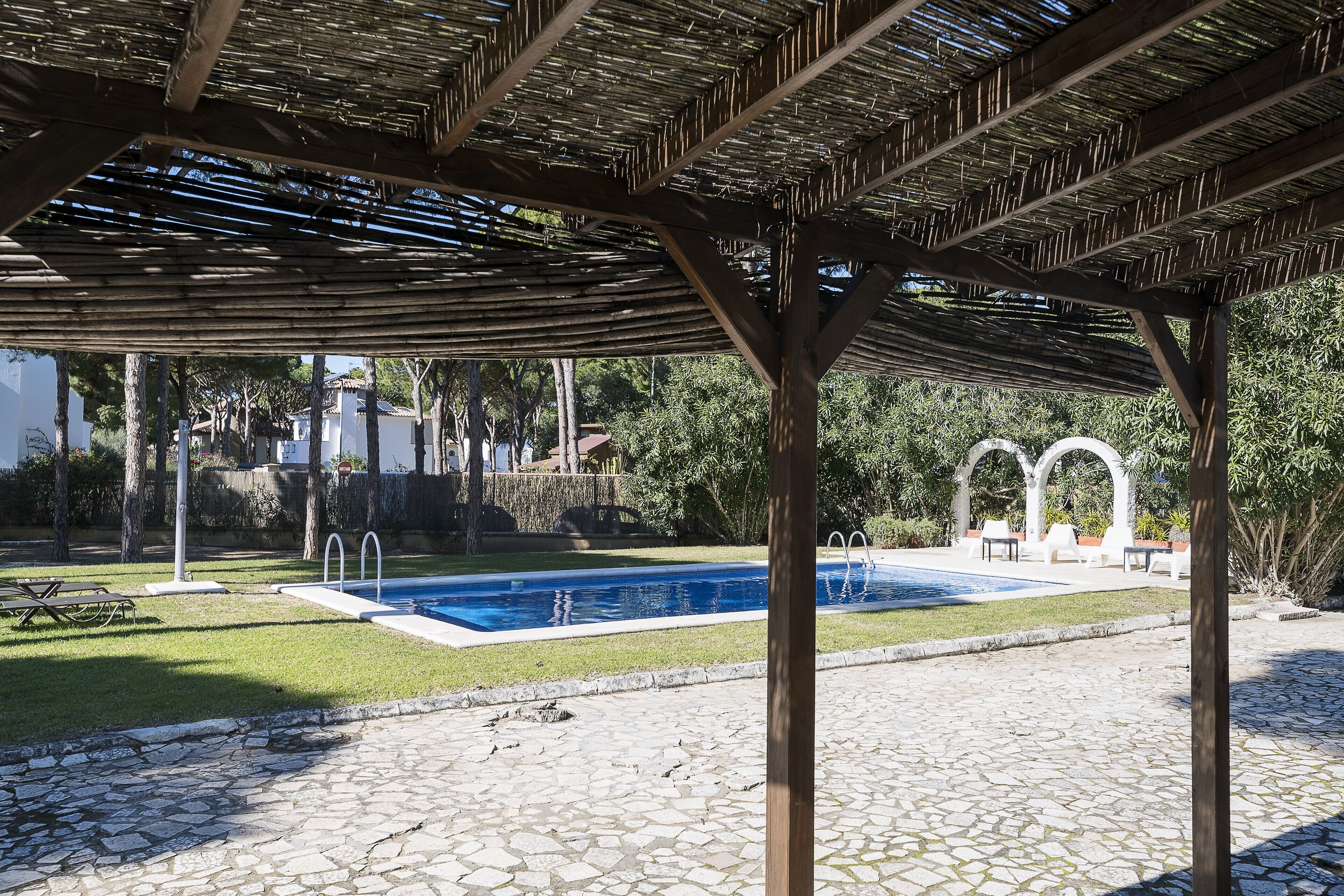 A covered swimming pool area with a stone-tiled deck, a pool, and a pergola structure.