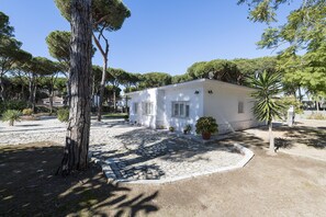 A white building with a stone-paved courtyard, surrounded by trees and potted plants. - Villa Pineda in Chiclana de la Frontera (Chiclana de la Frontera)