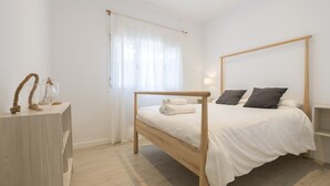 Un dormitorio minimalista con cama de madera, ropa de cama blanca y una mesita de noche con lámpara.